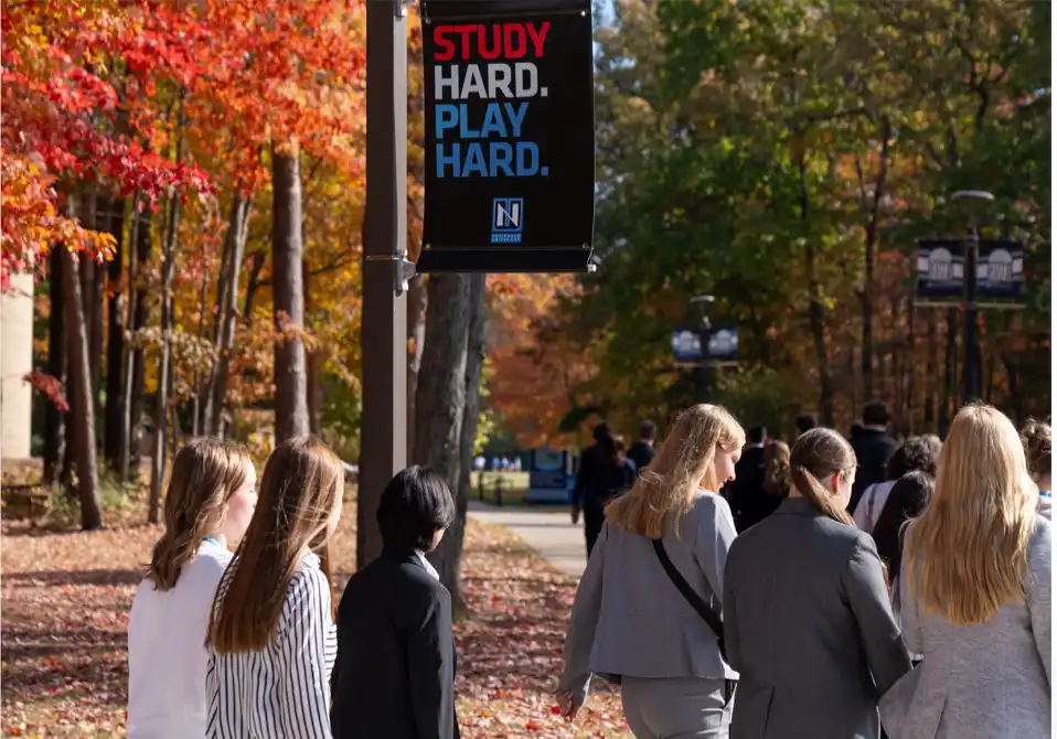 Northwood University students walking the Midland, Michigan campus in autumn beneath a 'Study Hard. Play Hard.' banner